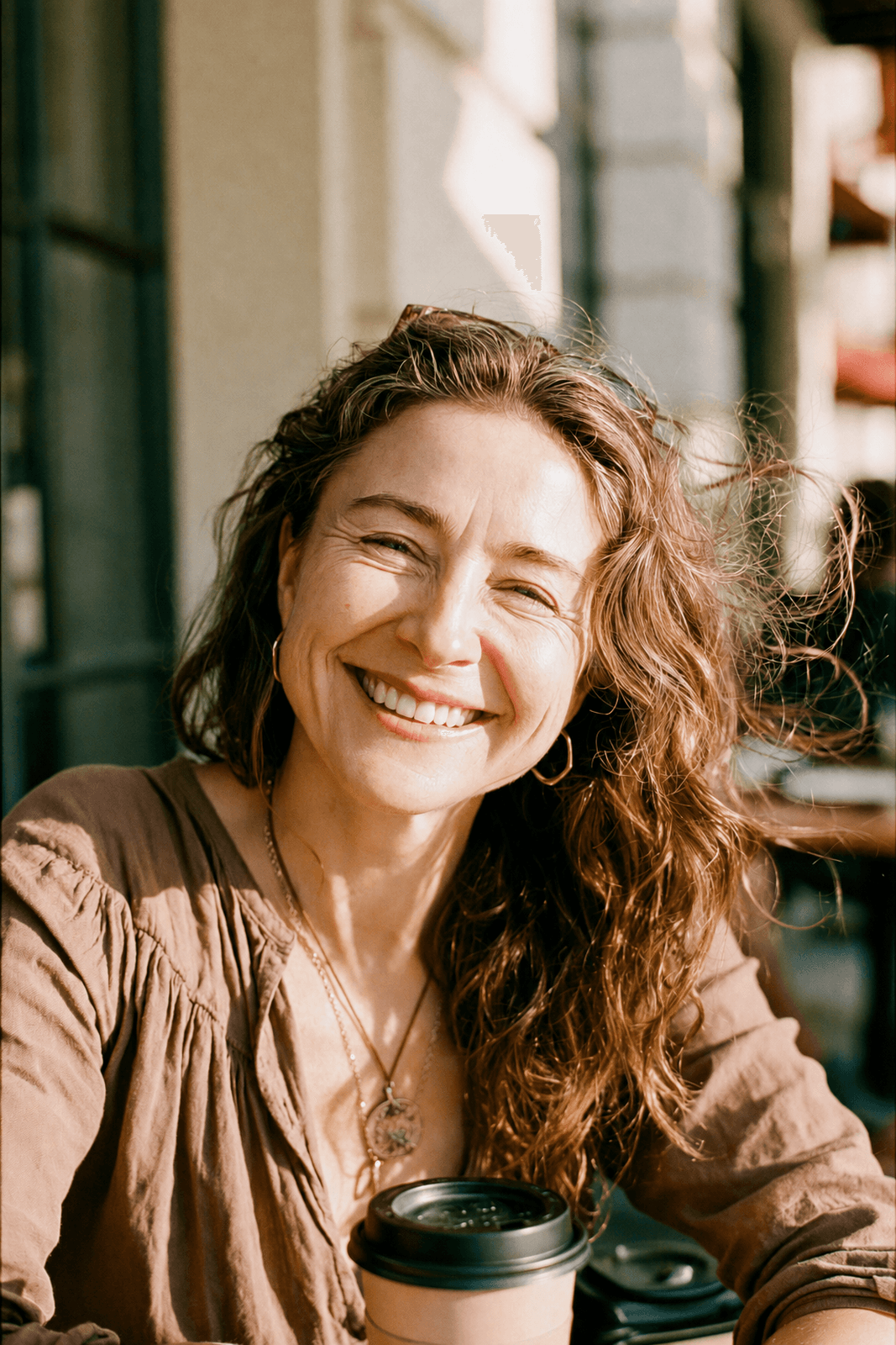 Teledris patient laughing with a coffee, hair caught in the breeze